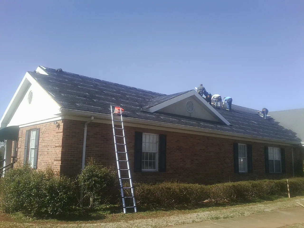 Crew tearing shingles off a brick ranch roof with a ladder set — Metal Roof Repair work by our crew in Jefferson City