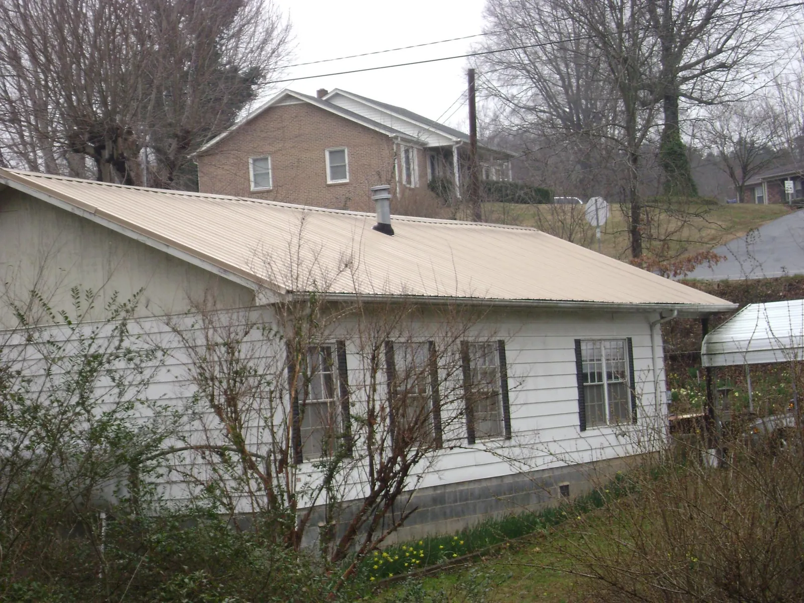 Tan metal roof on a white sided house set into a hillside — Commercial Roofing by Roofing Brothers in Jefferson City