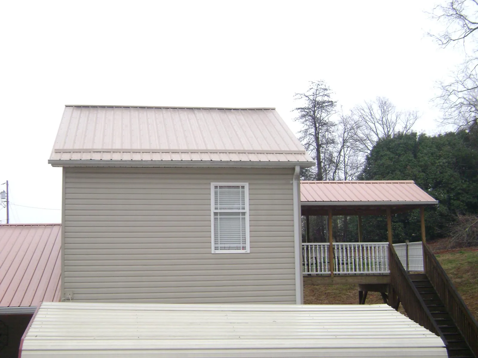 Tan metal roofs on a two story addition and attached porch, from a Roof Replacement job in Jefferson City